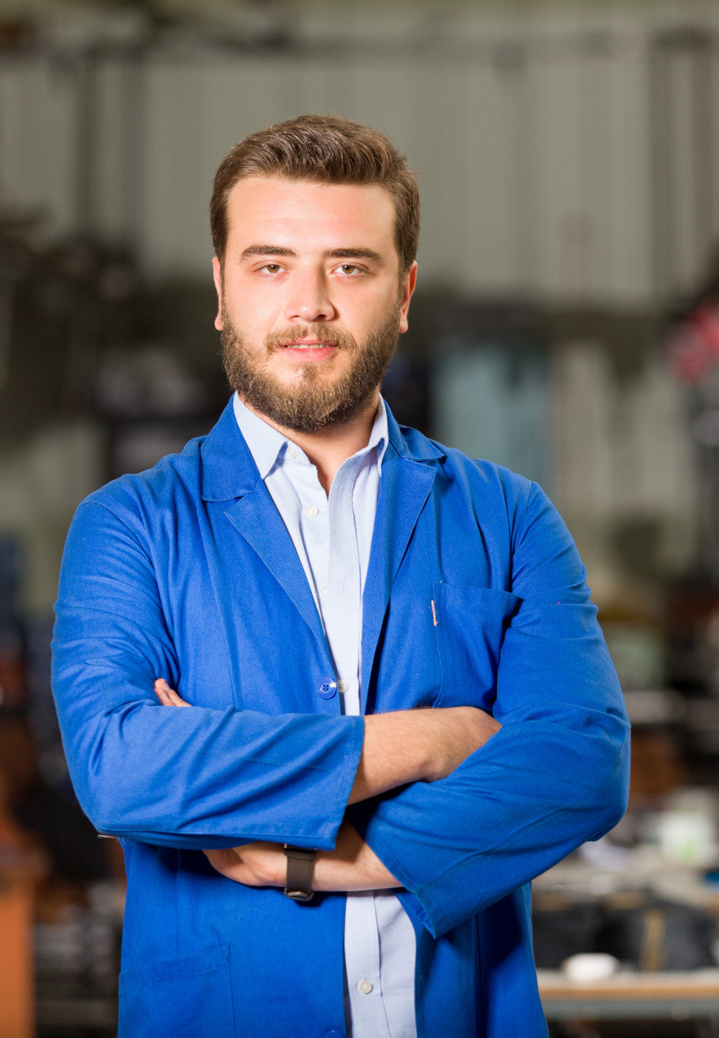 A man with a beard wearing a blue lab coat stan...