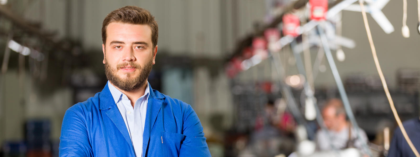 A man with a beard wearing a blue lab coat stan...
