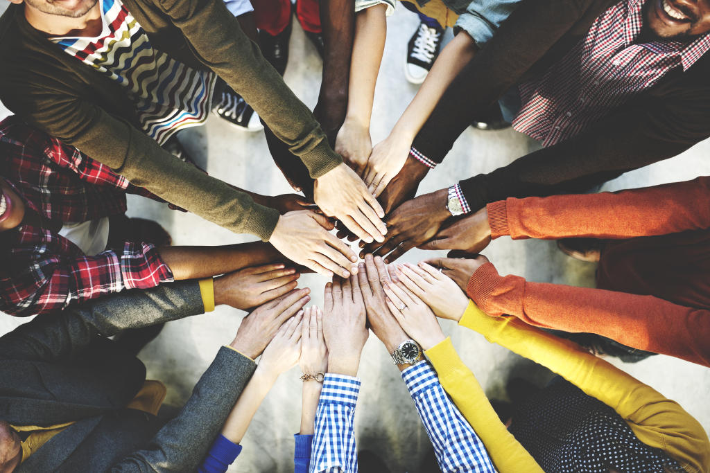 A diverse group of people standing in a circle with their hands joined in the...